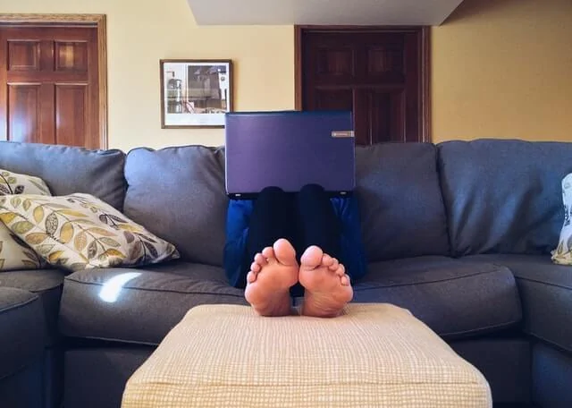 orang-sedang-berbaring-di-sofa-sambil-menopang-laptop-di-paha