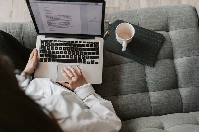 wanita memangku laptop sambil menulis sebelah secangkir kopi